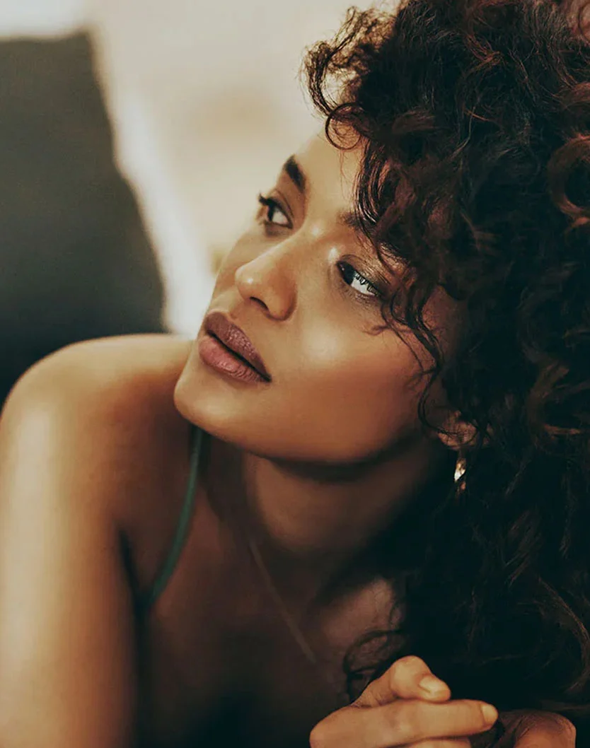 A portrait of a woman with curly brown hair, looking up and to the side. She is resting her chin on her hand and appears to be in a thoughtful pose. The lighting is soft and warm. - Kybella in Los Angeles, CA